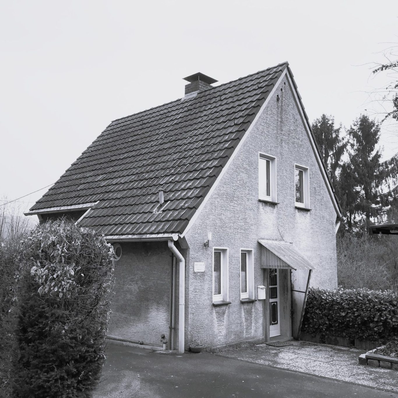 Ein hellgraues Haus mit Satteldach, umgeben von Bäumen und Sträuchern.