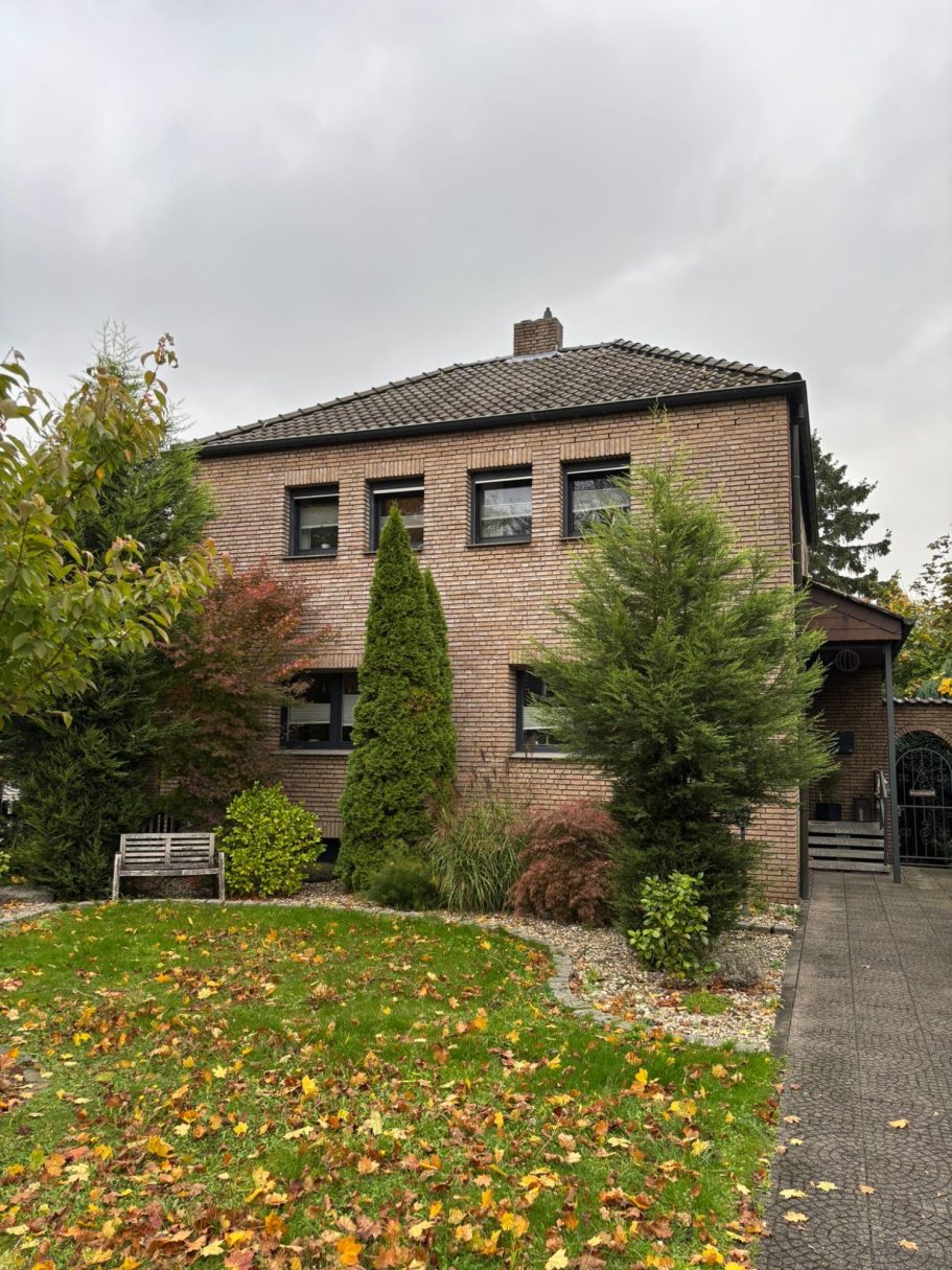 Bestandshaus Zweistöckiges Haus mit bräunlicher Fassade, Garten, Bänken und herbstlichem Laub.