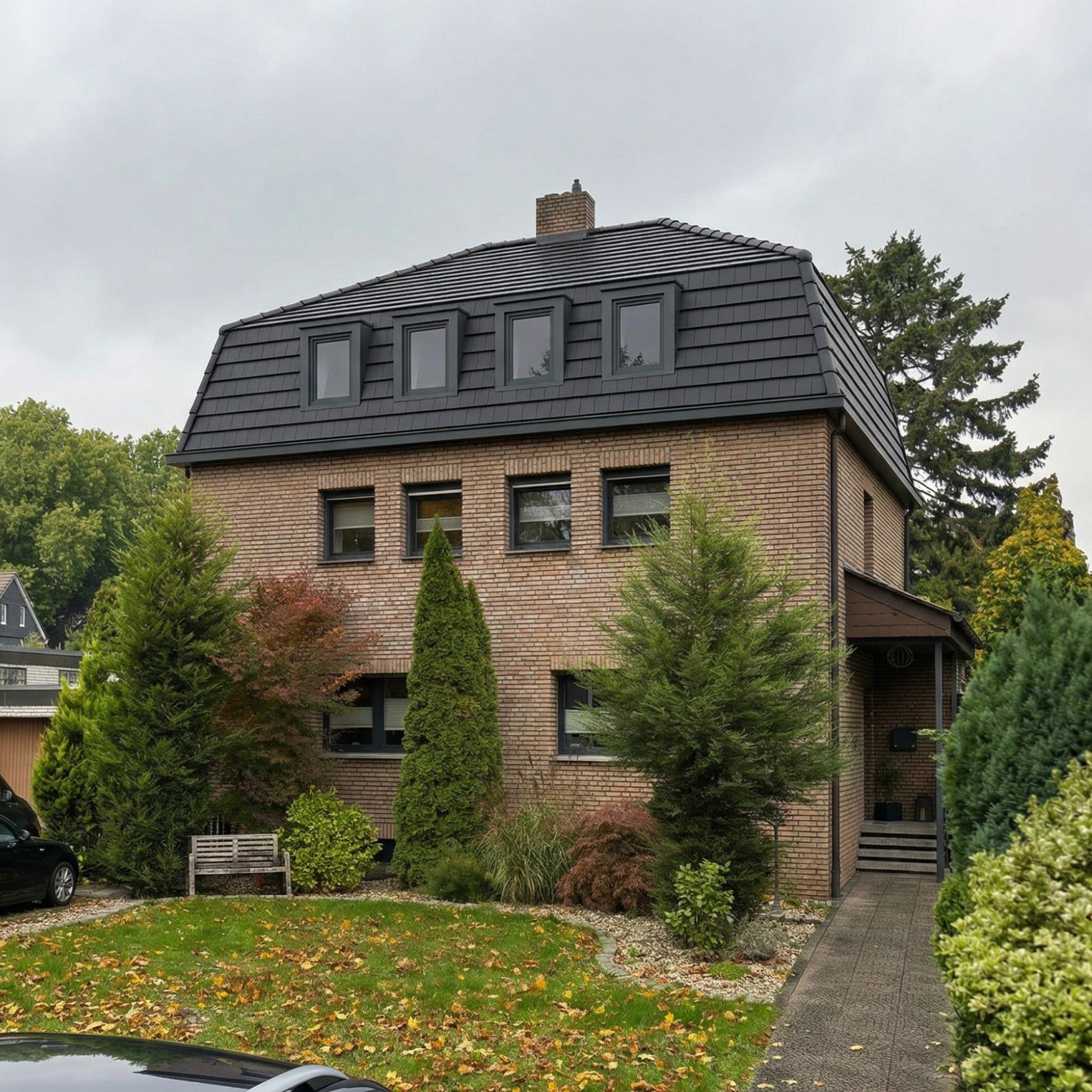 Projekt F7 Zweistöckiges, ziegelrotes Wohnhaus mit Garten und Bänken, umgeben von Bäumen.