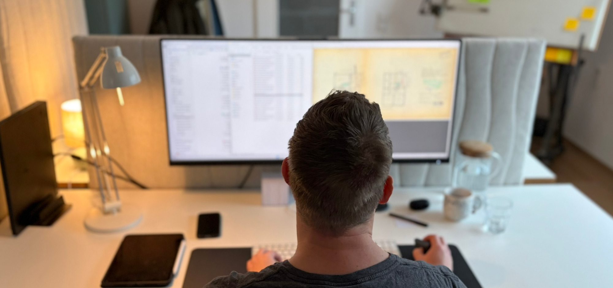 Person arbeitet am Schreibtisch mit mehreren Bildschirmen und digitalen Geräten.