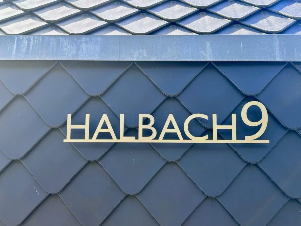 Hausnummer 9 mit dem Namen "HALBACH" in goldenen Buchstaben auf blauer Fassade.