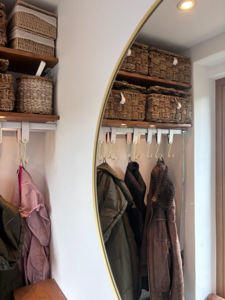 Wandspiegel neben einer Garderobe mit Kleidung und geflochtenen Körben.