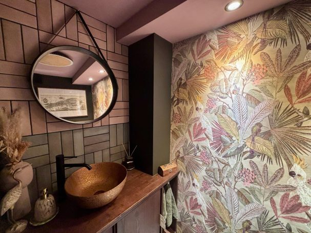Retro Badezimmer mit runden Spiegel, hölzernen Waschbecken und buntem Pflanzenmuster.